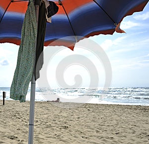 Under the umbrella on the beautiful Sabaudia beach. In the background an attractive woman sunbathing.