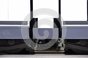 Undercarriage of a tram with white plating on the side and wheels that runs on the rails in a street