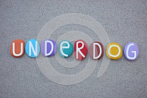 Underdog, creative text composed with multi colored stone letters over brown sand