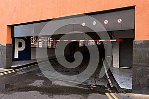 Underground car park entrance in a street of a residential or office building with P white sign on blue background and arrow.