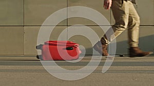 In an underpass or train station, a man in a hurry drops his red suitcase.