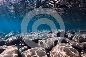 Undersea view with stones bottom, reflection in blue water. Ocean background