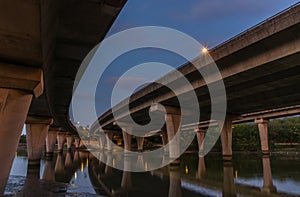 Underside of an elevated road across river at dusk