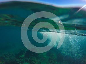 Underwater landscape with natural water split, blue sky above and green water below.