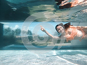 Underwater photo of aisan woman in bikini diving in the swimming pool with transparent glass wall. infinity pool edge on tropical photo
