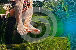 Underwater photo of child bare feet in natural swimming pool.