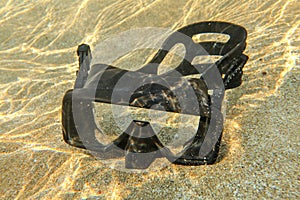 Underwater photo - light from sun refractions at black diving mask sitting in shallow water on clear sand