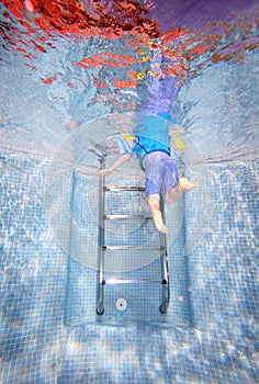 Underwater photo of young boy climbing out of swimming pool