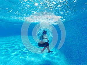 Underwater photography of little girl dives to the bottom of swimming pool