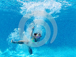Underwater photography of little girl dives to the bottom of swimming pool