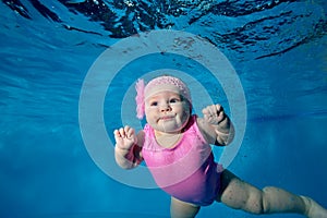 Underwater portrait of a charming baby girl swimming underwater in a children`s pool in a pink bathing suit on a blue