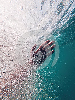 Underwater shot of emerging male hand in deep ocean water surrounded with air bubbles while swimming to the surface of the sea