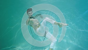 Underwater shot of man with a halfnaked torso wrapped in chains dancing modern ballet choreography. Male dancer moves in