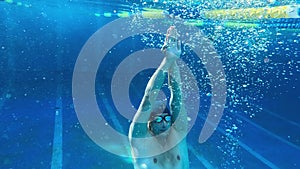 Underwater shot of a man swimming in a blue pool in natural sunlight