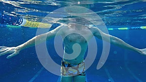 Underwater shot of a man swimming in a blue pool in natural sunlight