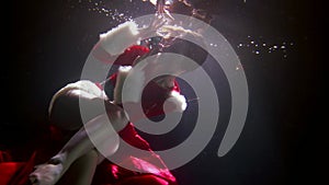 underwater shot with Xmas theme, young woman dressed red suit is holding magic shiny ball in hands