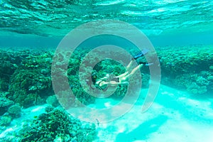 Underwater shot of the young lady gliding over vivid coral reef on a breath hold in sea water