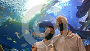 Underwater tunnel aquarium with Asian senior elder couple wear mask dating have fun happy together