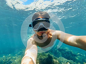 Underwater view of a diver man swimming in the turquoise sea under the surface with snorkelling mask taking a selfie