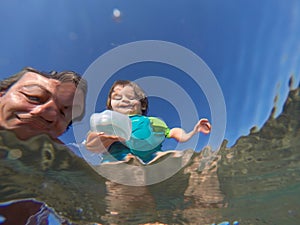 Underwater view of a father and her daughter with distorted faces having fun at the sea
