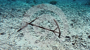 Underwater view of old rusty anchor at the bottom of a reef bottom in the ocean. An anchor welded from rebar overgrown