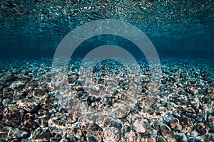 Underwater view with stones bottom and reflection on surface in ocean