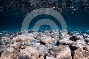 Underwater view with stones bottom, reflection in water. Ocean background