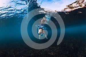 Underwater view of surfer girl with surfboard dive under barrel wave