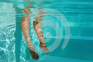 Underwater. Woman Keeping Legs In Pool While Sitting On Poolside. Female Enjoying Turquoise Water And Leisure At Resort.