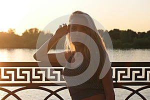 Undisturbed blond haired lady posing leaning at fence by hand in sunset light full of lovesikness