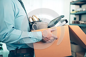 Unemployed hold cardboard box and resignation letter, dossier, alam clock, coffee cup, calculator and drawing tube in box. Quiting