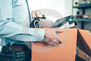 Unemployed hold cardboard box and resignation letter, dossier, alam clock, coffee cup, calculator and drawing tube in box. Quiting