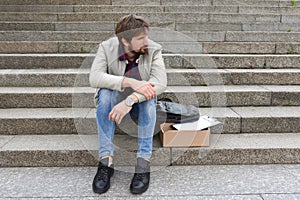 Unemployed man in depression sits on the stairs outdoors. Economic crisis, failure, despair. Unemployment and layoffs concept