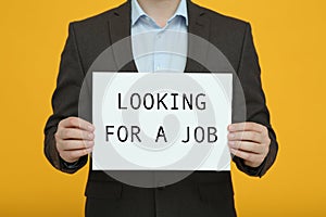 Unemployed man holding sign with phrase Looking For A Job on orange background, closeup