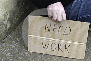 Unemployed man sitting on the ground holding the cardboard sign saying need work