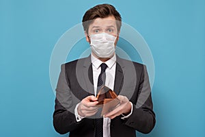 Unemployed sad man in medical mask and suit showing empty wallet