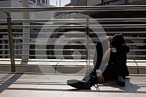 Unemployed stressed young Asian business man sitting on floor outdoors. Failure and layoff concept