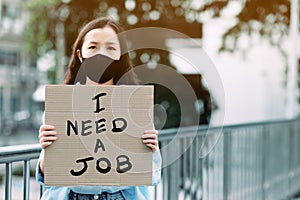 An unemployed women holding a paper sign writing a message saying she needs a job