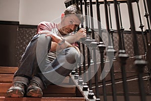 Unemployment and divorce - dramatic lifestyle portrait of sad and depressed man on his 40s sitting indoors on staircase thoughtful