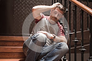 Unemployment and divorce - dramatic lifestyle portrait of sad and depressed man on his 40s sitting indoors on staircase thoughtful