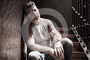 Unemployment and divorce - dramatic lifestyle portrait of sad and depressed man on his 40s sitting indoors on staircase thoughtful