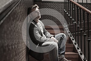 Unemployment and divorce - dramatic lifestyle portrait of sad and depressed man on his 40s sitting indoors on staircase thoughtful