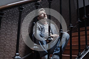 Unemployment and divorce - dramatic lifestyle portrait of sad and depressed man on his 40s sitting indoors on staircase thoughtful