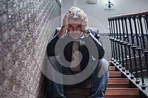 Unemployment and divorce - dramatic lifestyle portrait of sad and depressed man on his 40s sitting indoors on staircase thoughtful