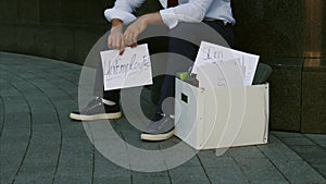 Unemployment, unemployed person, dismissal, downsizing. A man without a job. A young man sits on the street with a sign