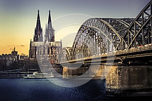 UNESCO Cathedral in Cologne Germany and Hohenzollern Bridge across Rhine River with Boat at Evening Sunset
