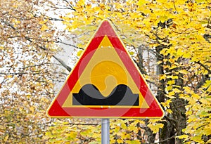 Uneven Road Sign on yellow autumn leaves background.