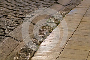 Uneven surface of textured low curb for rainwater runoff in evening street lighting