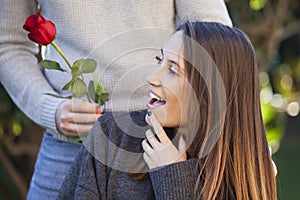 Unexpected moment in routine everyday life! Cropped photo of man`s hands holding a red rose. The happy woman is looking at the gif