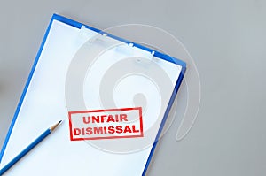 Unfair dismissal written on notepad with paper and pencil on grey background